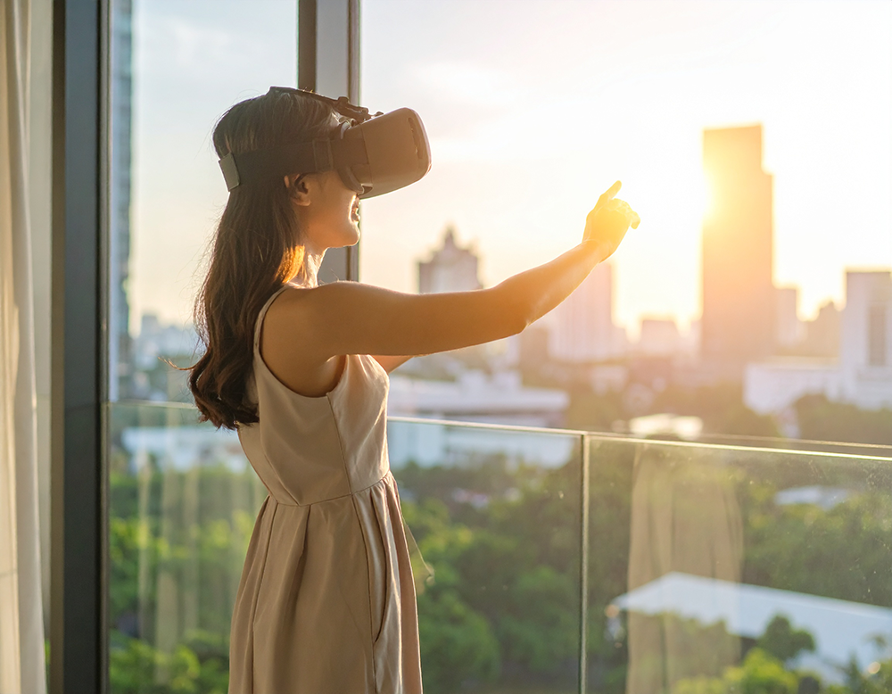 都市の夕焼けが見える部屋でVRゴーグルを装着する女性。