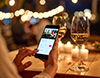 夜のレストランで、スマートフォンでオンラインショッピングをする女性の手元。