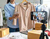 スマートフォンを三脚に固定し、洋服をライブ配信で販売する女性。