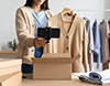 段ボール箱の横で、スマートフォンで洋服を撮影する女性。