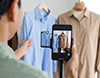 スマートフォンでハンガーにかかった洋服を撮影する男性。