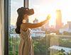 都市の夕焼けが見える部屋でVRゴーグルを装着する女性。
